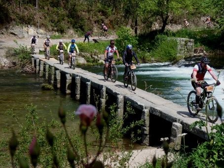 ciclistas a atravessar ponte de pedra sobre o rio