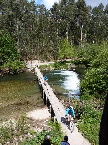 ciclistas a atravessar ponte de pedra sobre o rio
