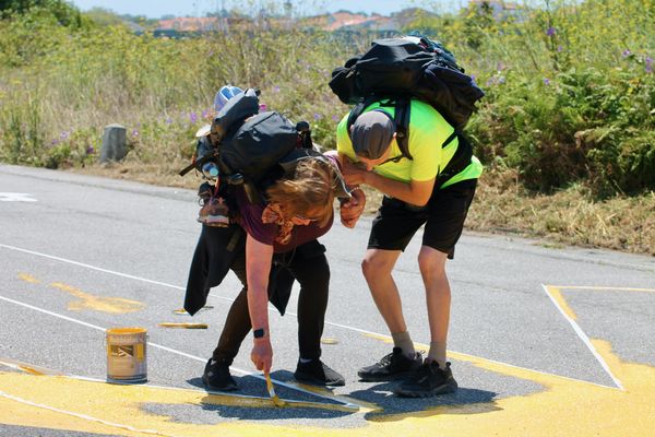 dois peregrinos a pintar uma seta amarela na estrada