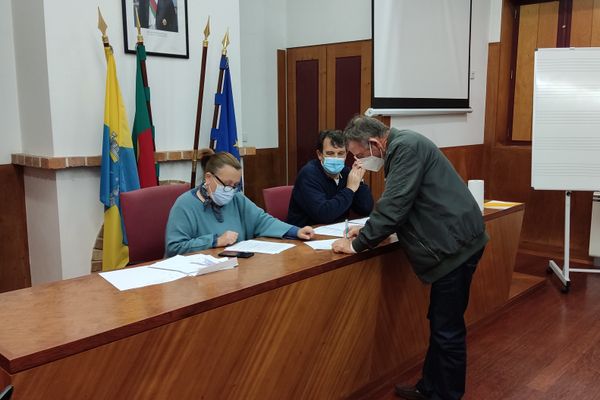 três pessoas, uma a assinar um papel