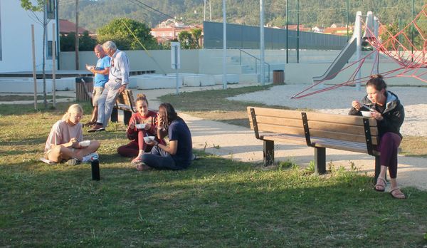 várias pessoas sentadas em bancos, num parque, a comer sopa